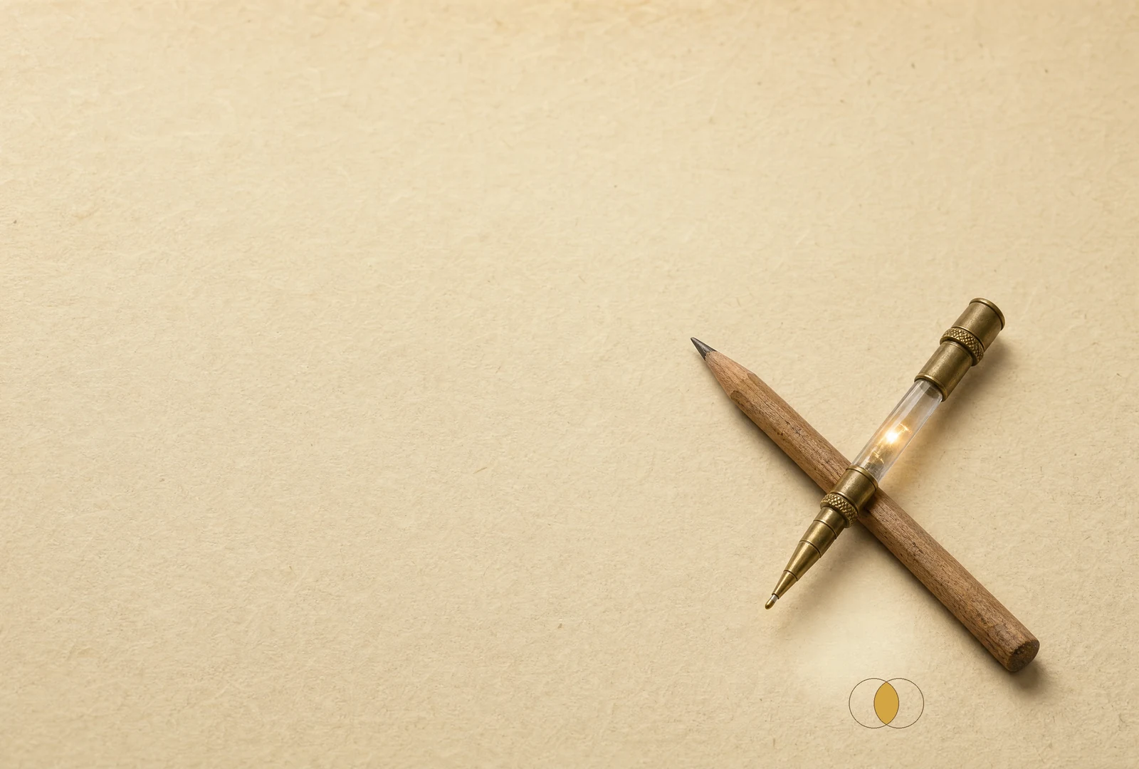 A wooden pencil crosses a brass-and-glass stylus. Beneath them, two equal circles overlap around a gold almond-shaped centre.